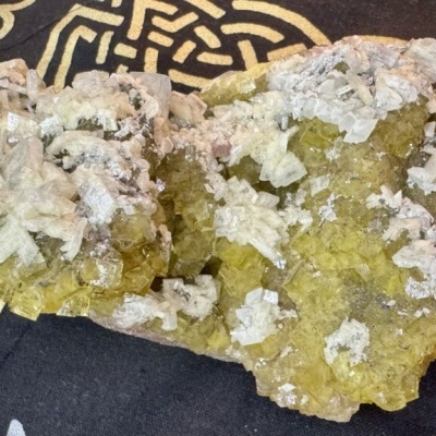 Cristal mineral amarelo com cristais brancos sobre fundo preto com padrão dourado