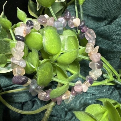 Pulseira de pedras naturais em tons rosa e roxo sobre folhagem verde e tecido escuro