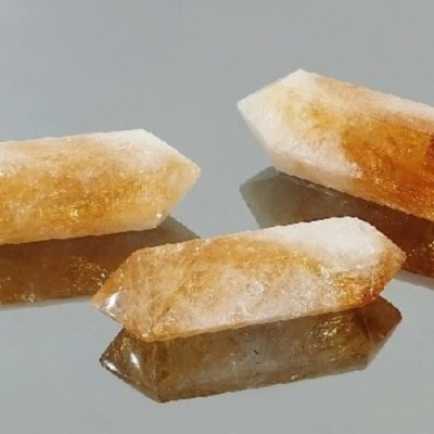 Três cristais de quartzo citrino amarelo e branco sobre superfície espelhada cinzenta