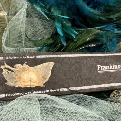 Caixa preta de incenso Frankincense decorada com flor himalaia sobre tecido azul e penas verdes