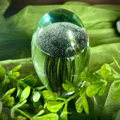 Objeto decorativo em vidro com padrão preto e branco sobre tecido verde e folhas verdes
