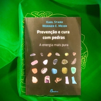 Livro sobre prevenção e cura com pedras sobre tecido verde bordado.