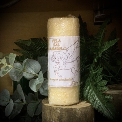 Vela amarela com rótulo de cavalo alado sobre tronco de madeira e folhas verdes