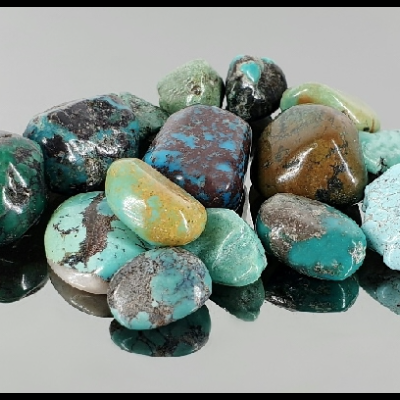Pedras semipreciosas polidas em tons de verde, azul e castanho sobre fundo cinzento