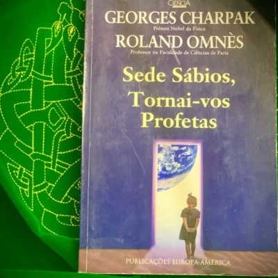 Livro com capa azul escuro e texto amarelo sobre fundo verde bordado