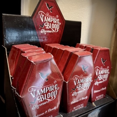 Caixas vermelhas em forma de caixão com texto Vampire Blood Incense e morcego preto em expositor preto.