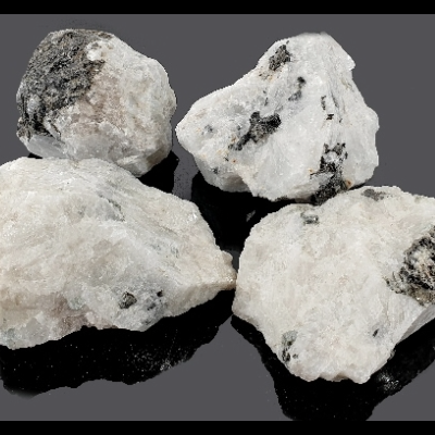 Quatro pedras minerais brancas com manchas pretas sobre fundo preto