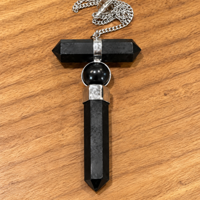 Colar com pendente em forma de cruz em pedra negra e metal prateado sobre madeira clara