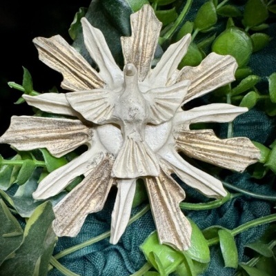 Adorno decorativo branco e dourado com forma de sol e pássaro sobre tecido verde e folhas