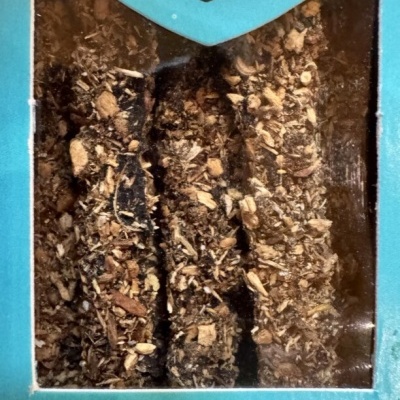 Caixa azul com três bastões de incenso de arruda cobertos com partículas vegetais.