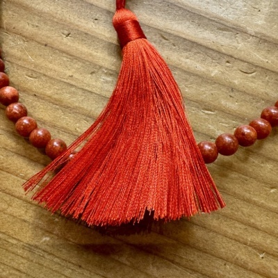 Colar de contas vermelhas com pendente de franjas vermelhas numa superfície de madeira clara