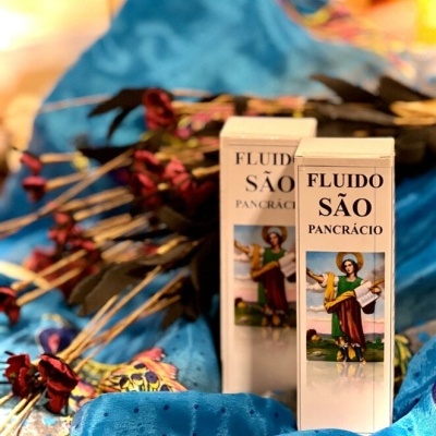 Duas caixas brancas de fluido São Pancrácio com imagem de santo, sobre tecido azul e flores secas vermelhas e pretas.