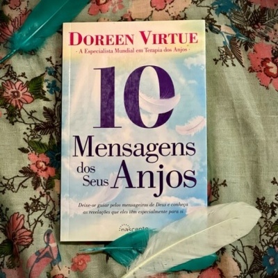 Livro 10 Mensagens dos Seus Anjos sobre tecido floral com três penas ao redor