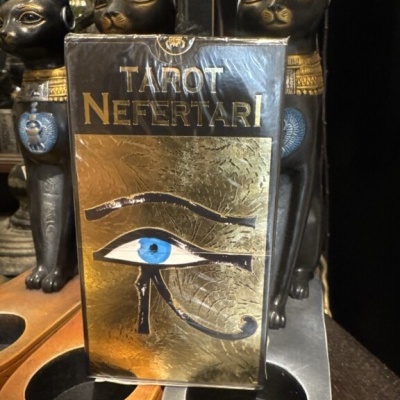 Embalagem do baralho Tarot Nefertari com o Olho de Hórus azul, entre estátuas de gatos e suportes para objetos