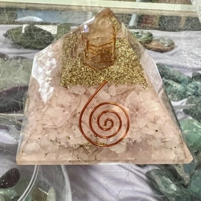 Pirâmide decorativa de resina com pedras rosas, detalhes dourados e fio de cobre em espiral.