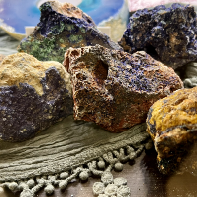 Pedras brutas coloridas em cima de tecido cinza com franjas