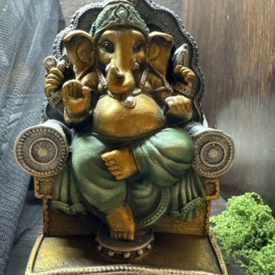 Estátua de Ganesha dourada e verde sentada numa cadeira decorativa