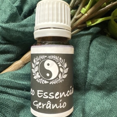 Frasco de óleo essencial de gerânio com etiqueta preta e símbolo yin-yang sobre pano verde
