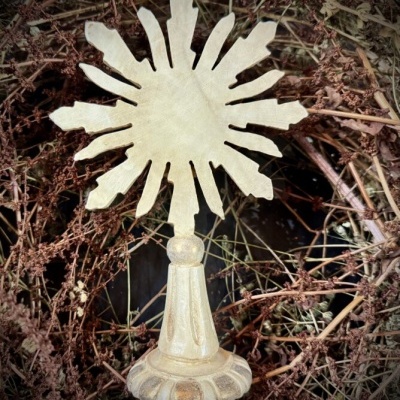 Escultura dourada em forma de sol sobre coroa de ramos secos