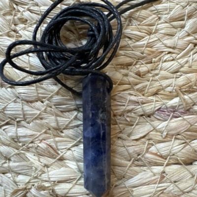 Colar com pendente de cristal azul e cordão preto sobre esteira de palha