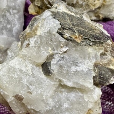 Minerais brancos com inclusões castanhas e pretas sobre tecido roxo
