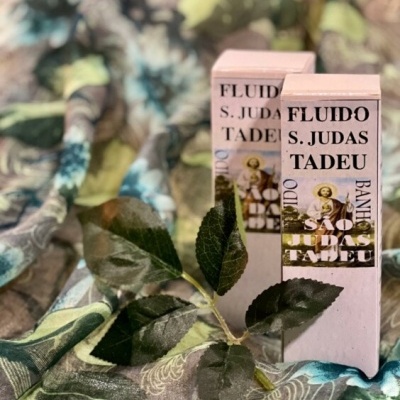 Duas embalagens retangulares de fluido São Judas Tadeu com folhas verdes falsas e tecido estampado ao fundo.