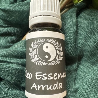 Frasco de óleo essencial Arruda com rótulo preto e símbolo yin-yang em tecido verde.