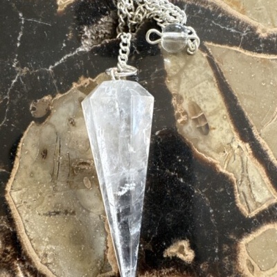Pingente de cristal transparente com corrente prateada sobre superfície marmorizada