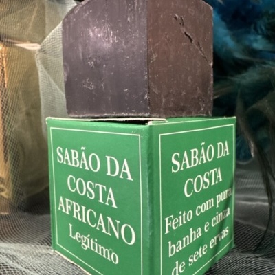 Sabonete castanho escuro em cima de caixa verde com texto branco sobre tecido translúcido