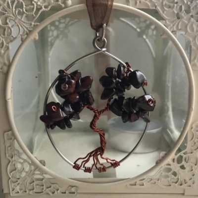Pendente decorativo árvore de arame e pedras negras em moldura branca com padrão floral.