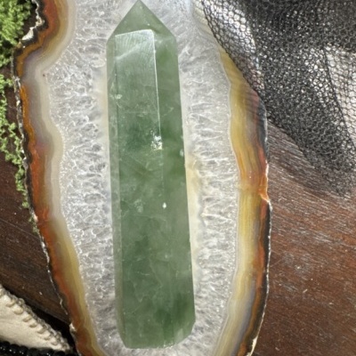 Cristal verde polido sobre base de ágata com camadas coloridas, em superfície de madeira com tecido e contas.