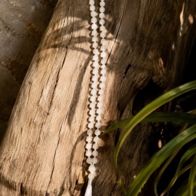 Colar de contas brancas com tassel sobre madeira rústica