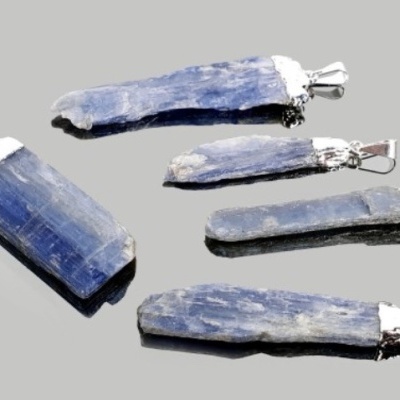 Cinco pendentes de pedra azul kyanite com metal prateado sobre superfície cinzenta refletora