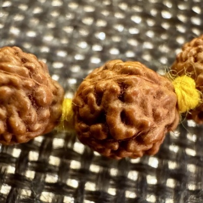 Contas de madeira castanhas em cordão amarelo sobre tecido quadriculado preto e branco