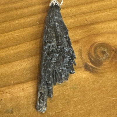 Pingente de cristal negro bruto com aro metálico prateado em fundo de madeira clara