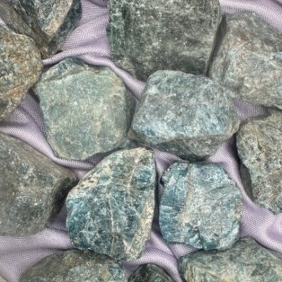 Pedras brutas verdes e cinzentas sobre tecido violeta claro