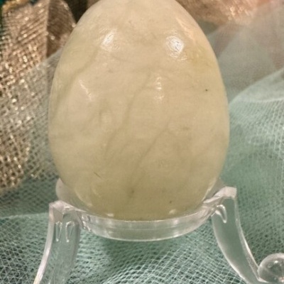 Ovo decorativo de pedra esbranquiçada em suporte transparente sobre tecido dourado e verde