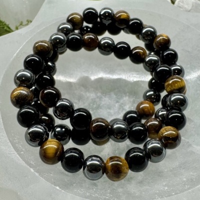 Colar ou pulseira de contas castanhas, pretas e douradas sobre superfície branca