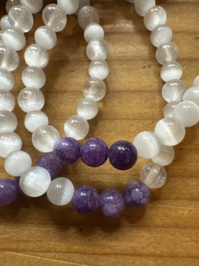 Pulseiras com contas brancas translúcidas e roxas numa superfície de madeira clara