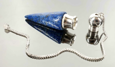 Pêndulo de cristal azul com base metálica e corrente prateada sobre superfície espelhada