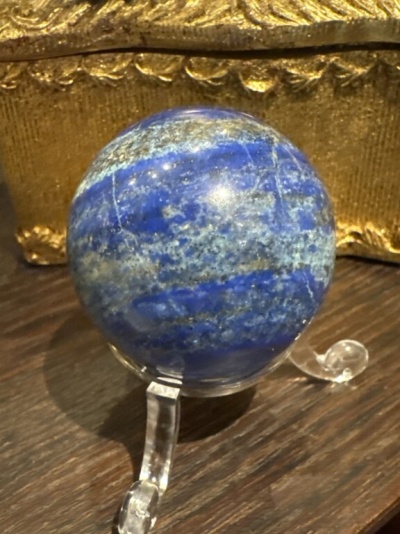 Esfera azul em suporte transparente sobre madeira e fundo dourado