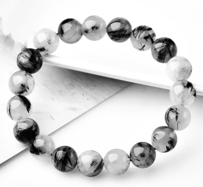 Pulseira de contas esféricas transparentes com inclusões negras sobre fundo branco e cinza claro