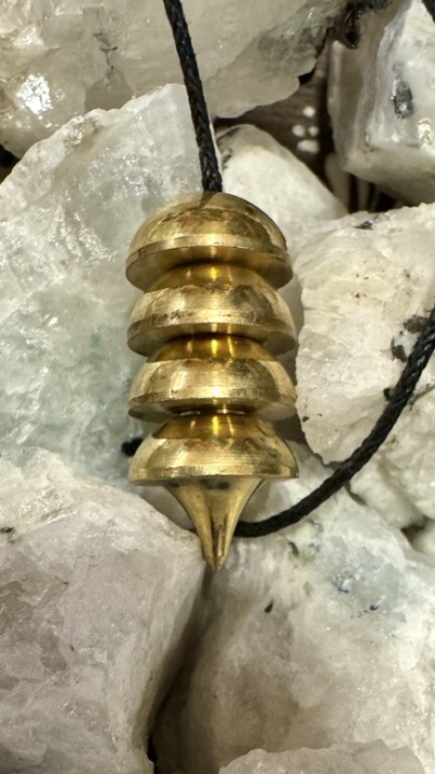 Pêndulo dourado com discos empilhados e cordão preto sobre pedras translúcidas