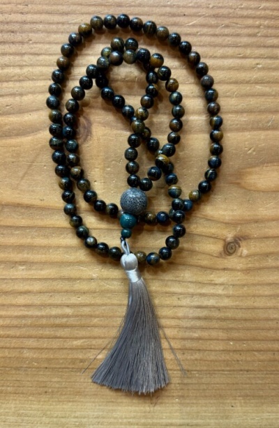 Colar de contas castanho e preto com tassel cinzento sobre madeira clara