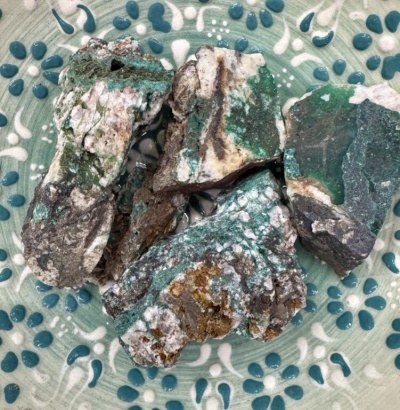 Pedras rústicas verdes e brancas sobre prato decorativo verde com padrão branco e azul