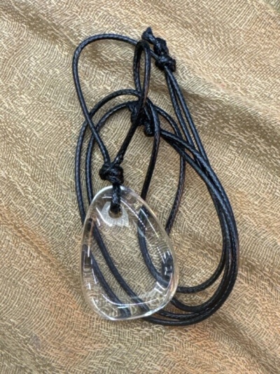 Colar com pendente de vidro transparente e cordão preto sobre tecido castanho