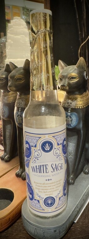 Frasco de água de limpeza White Sage com estátuas de gatos egípcios ao fundo