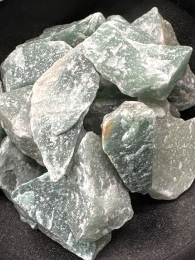 Pedras brutas verdes e brancas em superfície escura.