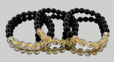 Três pulseiras de contas pretas e transparentes amarelas sobre superfície espelhada cinza.