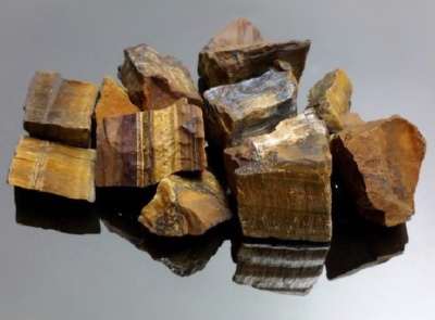 Pedras brutas castanhas e douradas com textura estriada num fundo preto refletor